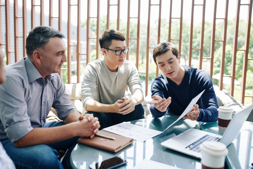 Financial department manager explaining figures in report to his colleagues at meeting